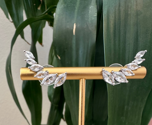 Gold earring stand with leaf-shaped earrings against a plant background