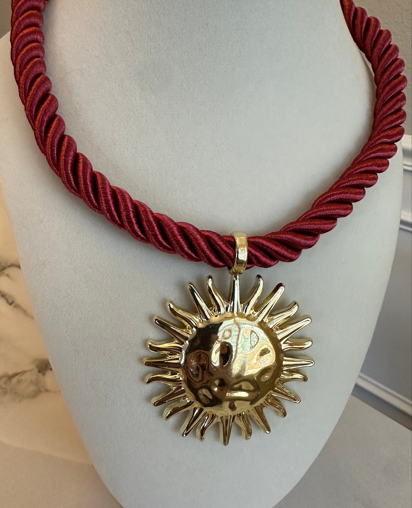 Red braided cord with a gold sun-shaped pendant on a white mannequin bust.