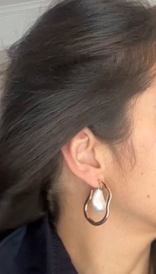 Woman with dark hair and earrings, wearing a dark coat indoors.