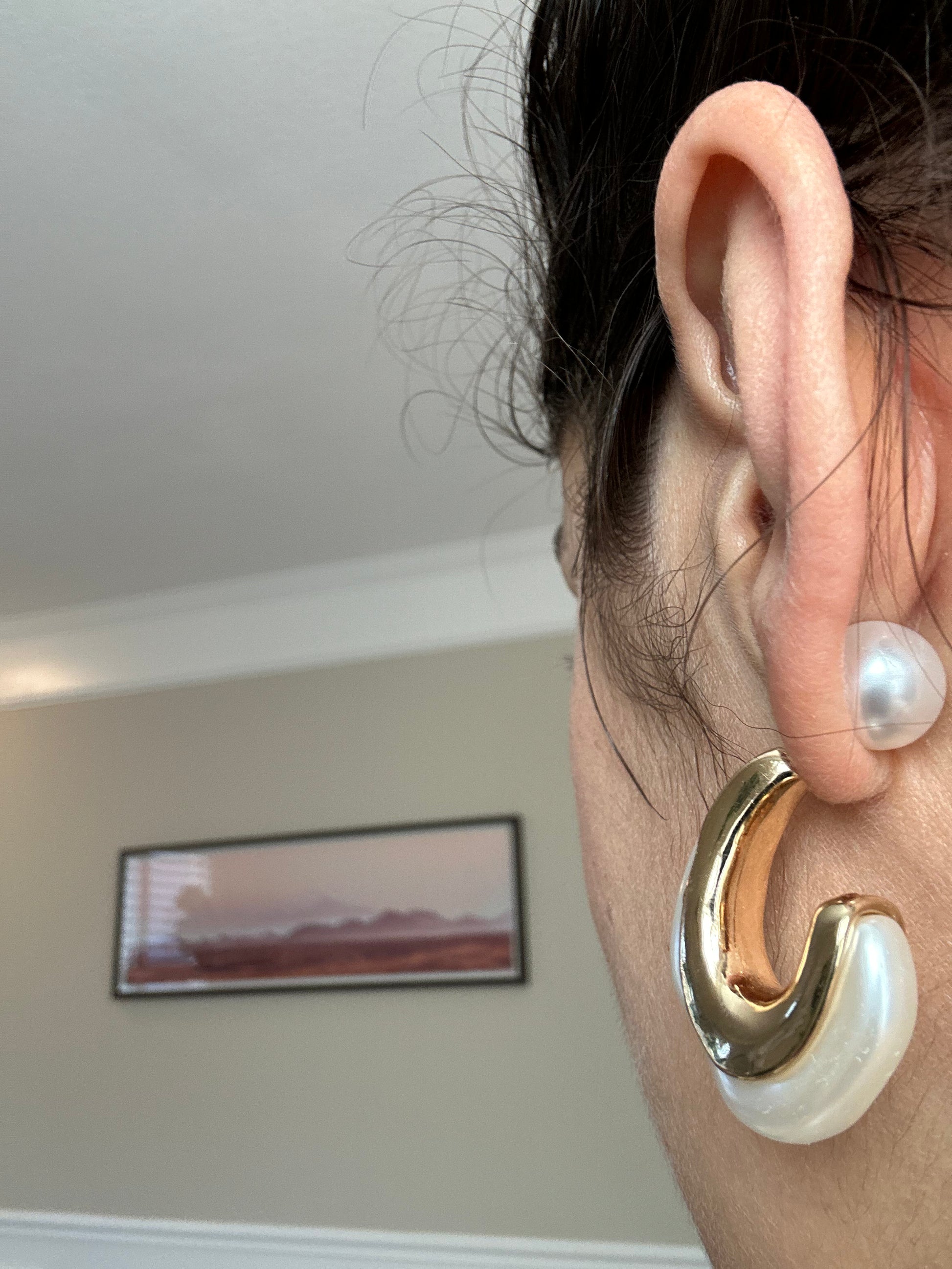 Gold and pearl earring worn by a person with a blurred indoor background