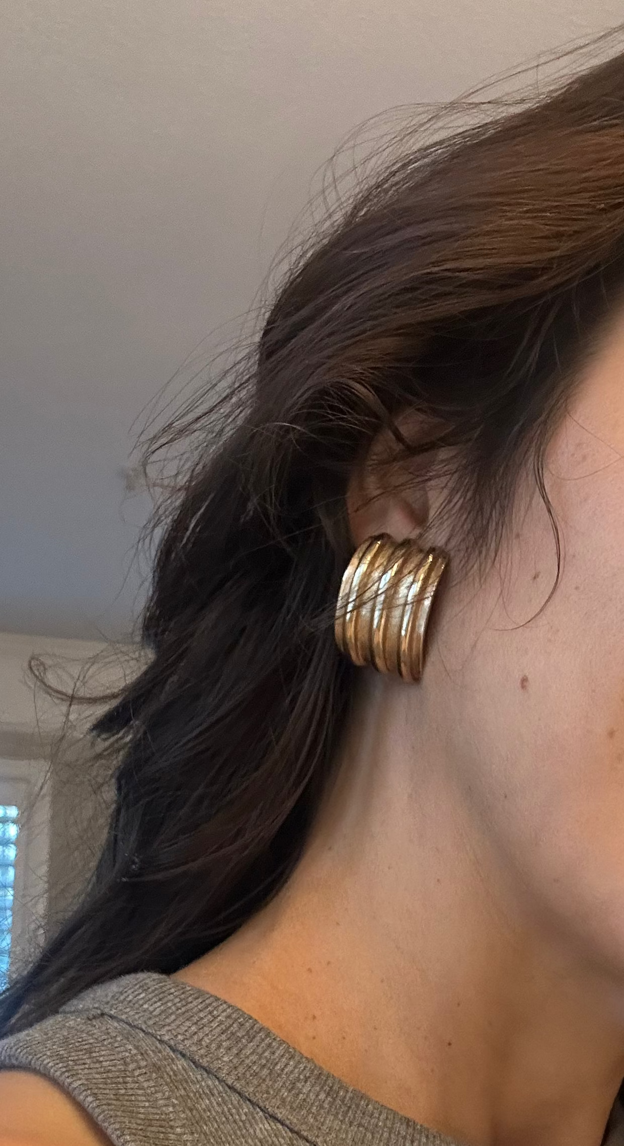 Woman wearing gold hoop earrings indoors with a neutral background