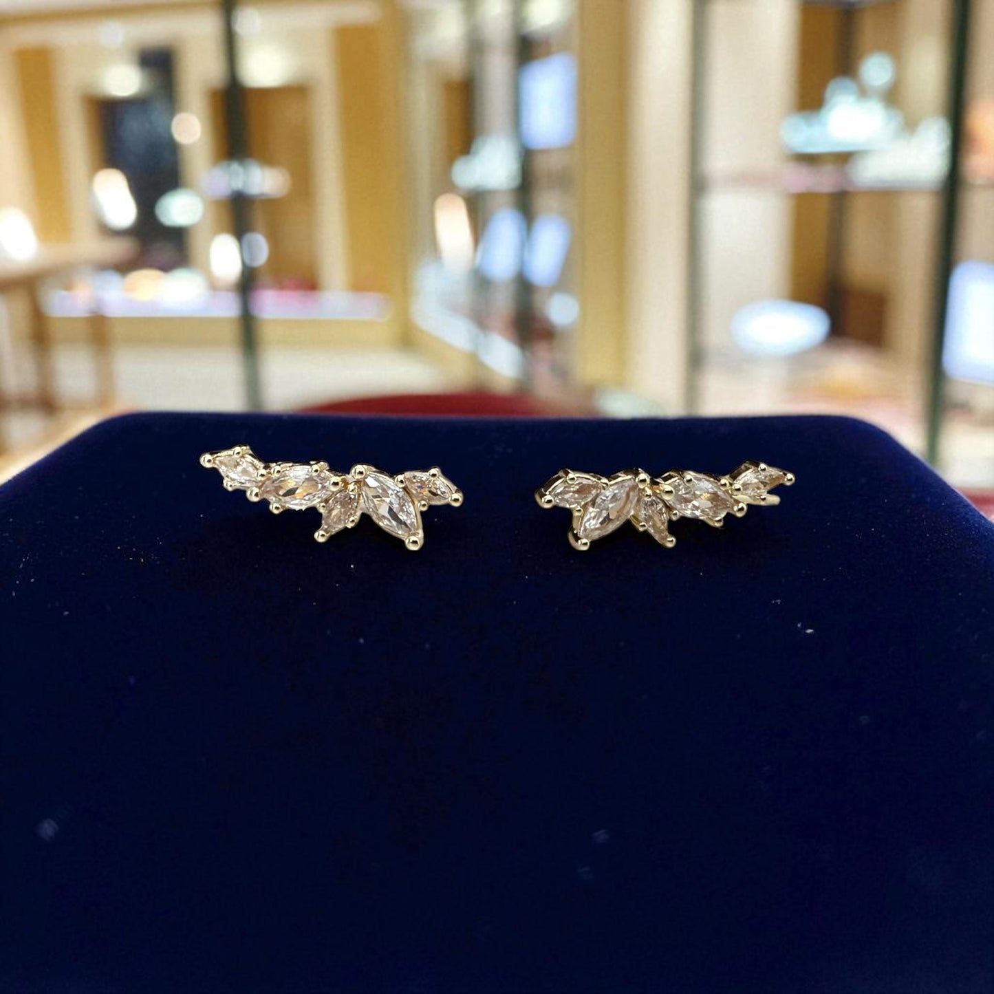 Pair of gold earrings on a blue cushion with a blurred indoor background