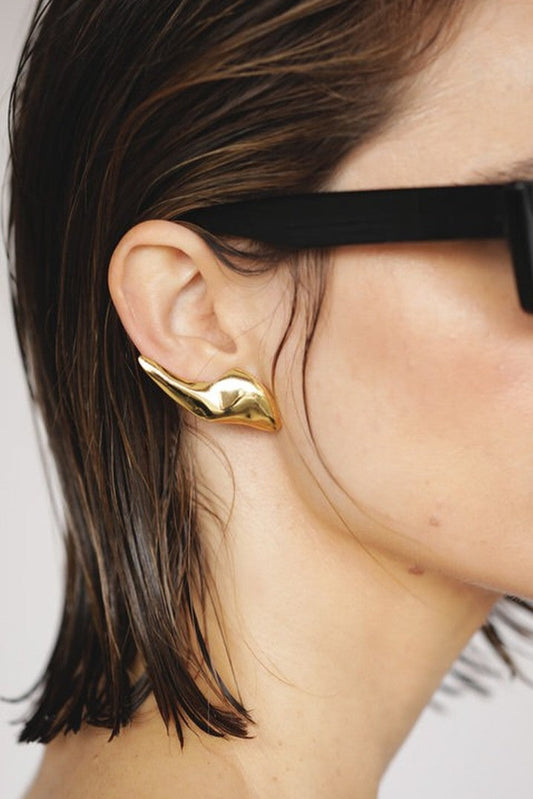 Woman wearing black sunglasses and a gold earring on a plain background