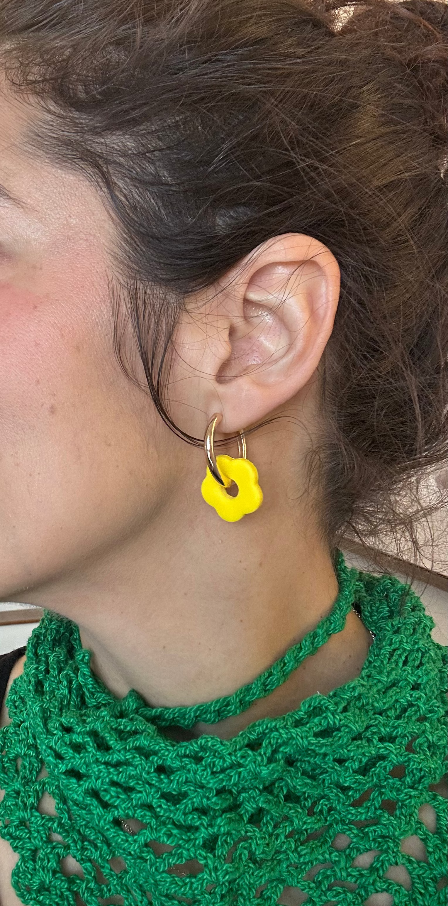 Woman wearing a green crochet scarf and yellow flower earrings indoors.