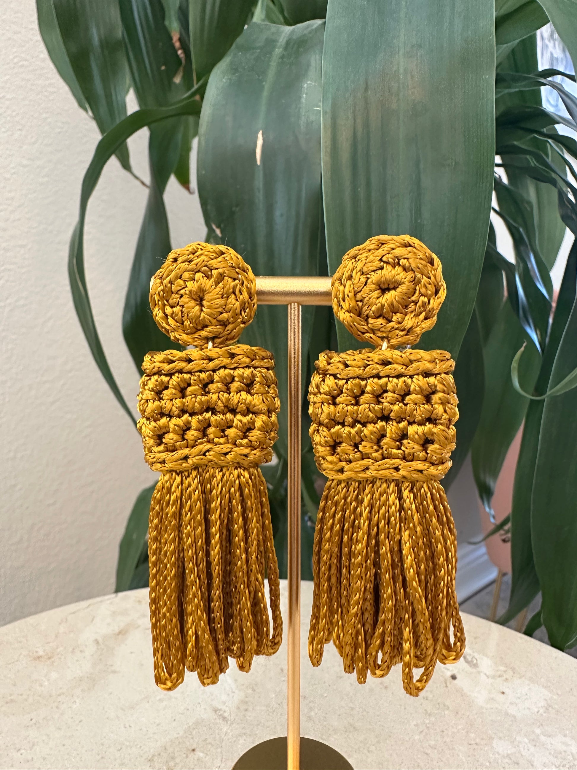 Gold tassel earrings on a stand with a green leafy background