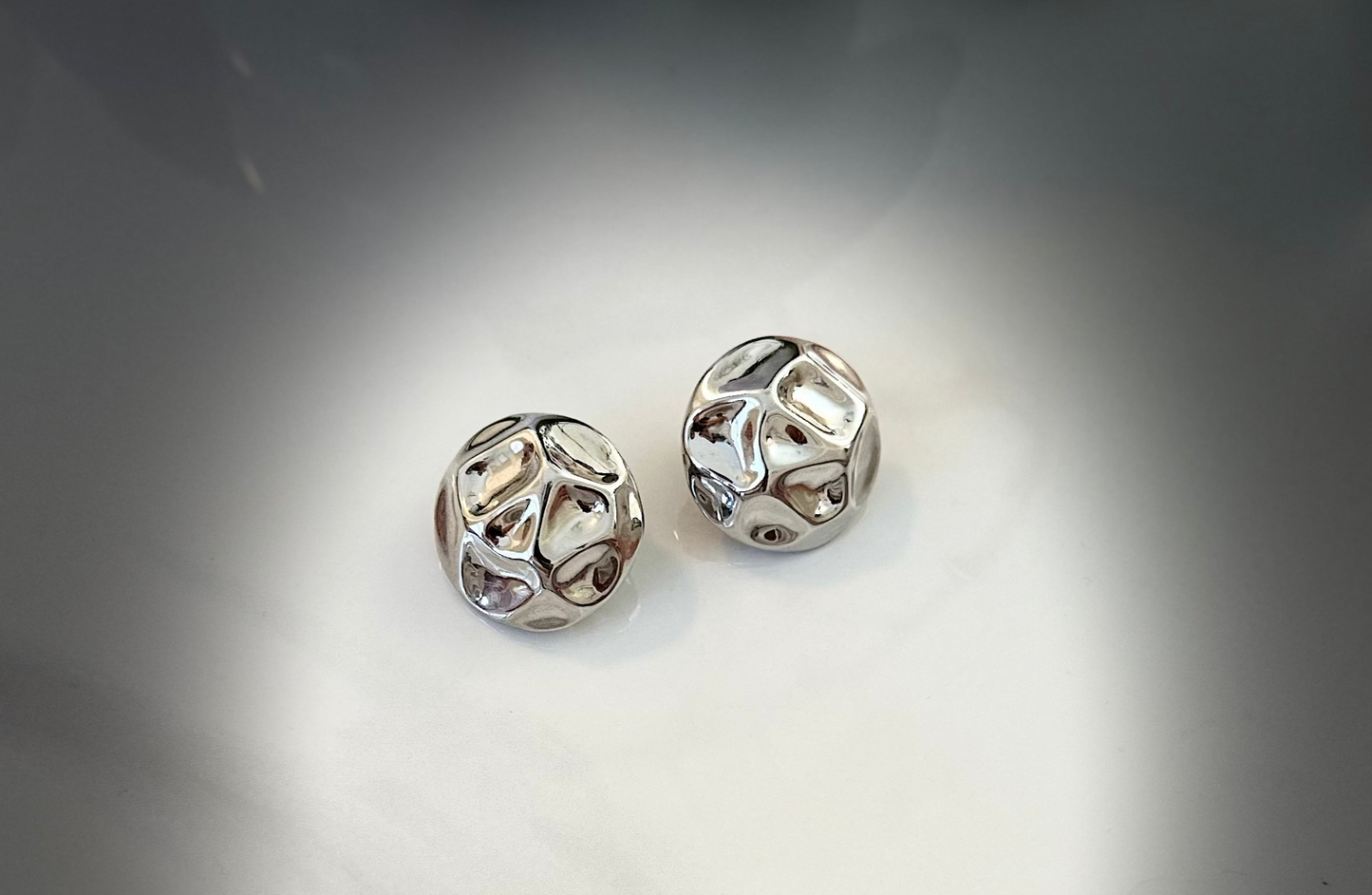 Pair of silver earrings on a reflective surface