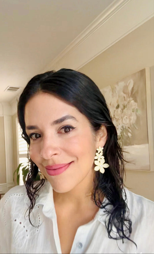 Woman wearing a white blouse with floral earrings in a room with a painting on the wall.