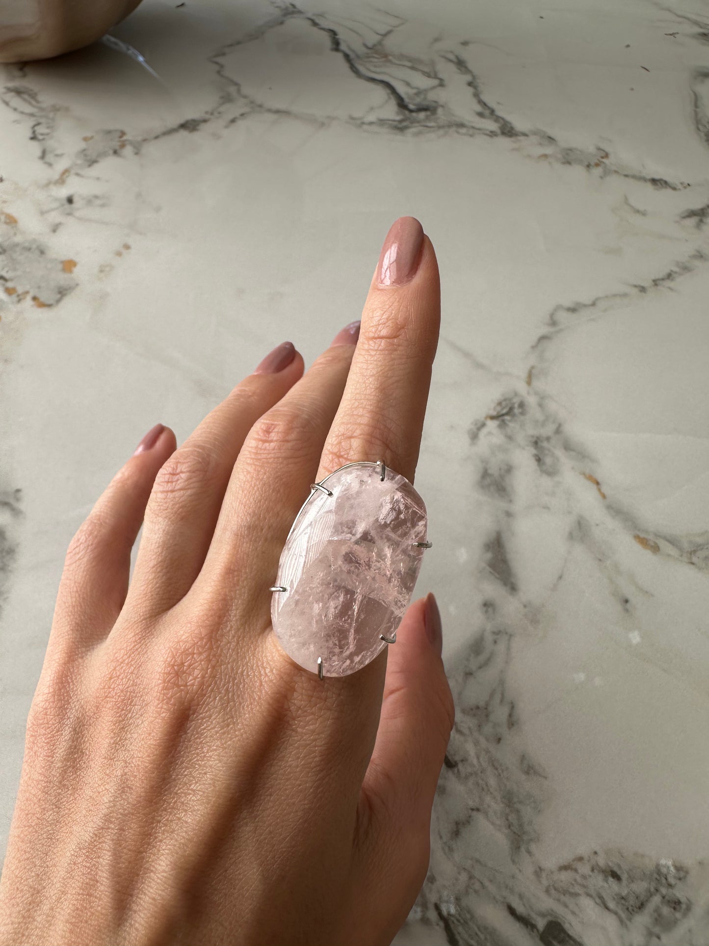 Hand wearing a large, ornate ring on a marble surface