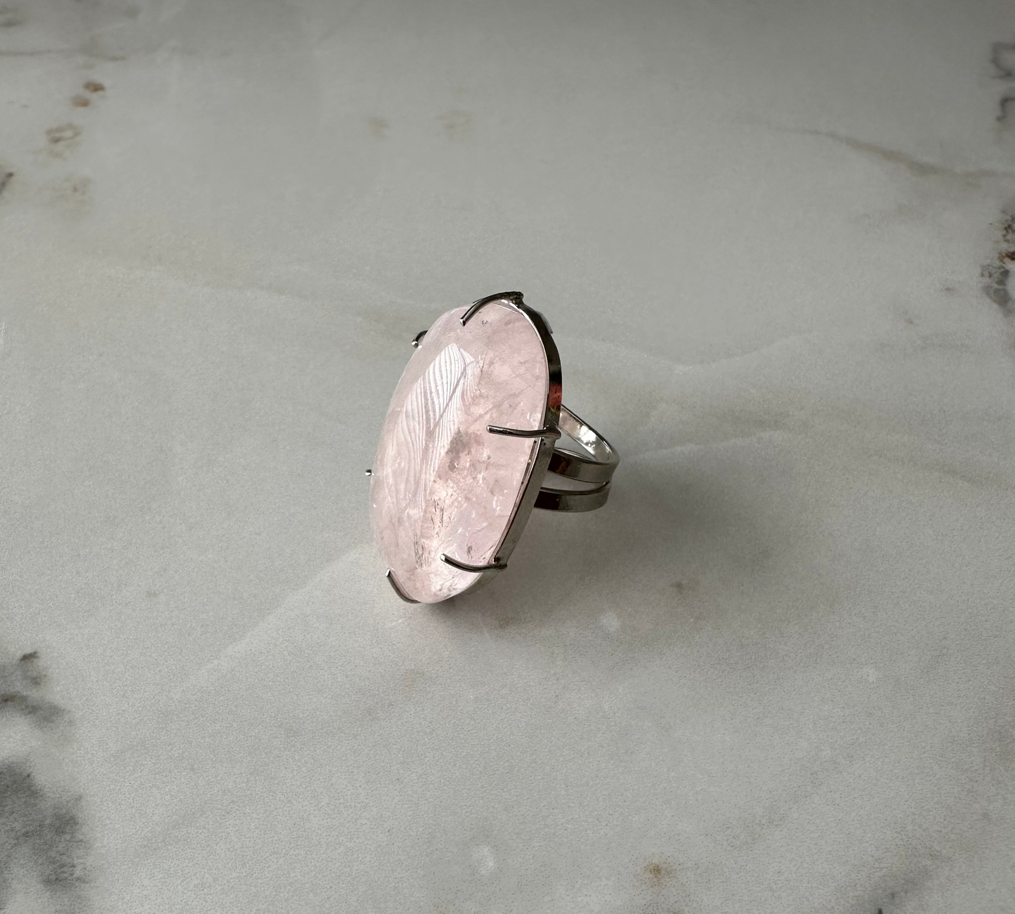 Silver ring with a large, oval-shaped stone on a marble surface