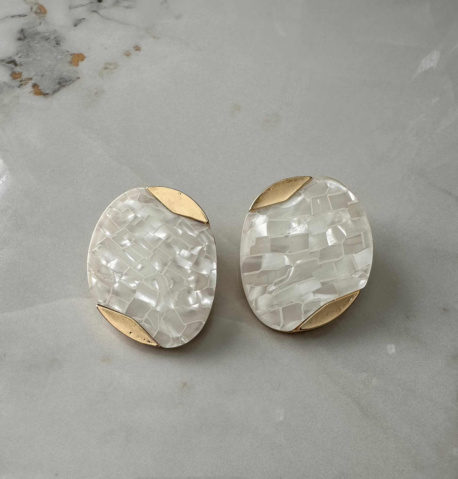 Pair of earrings with gold and white stone design on a marble surface