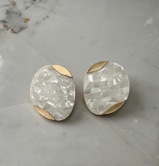 Pair of earrings with gold and white stone design on a marble surface