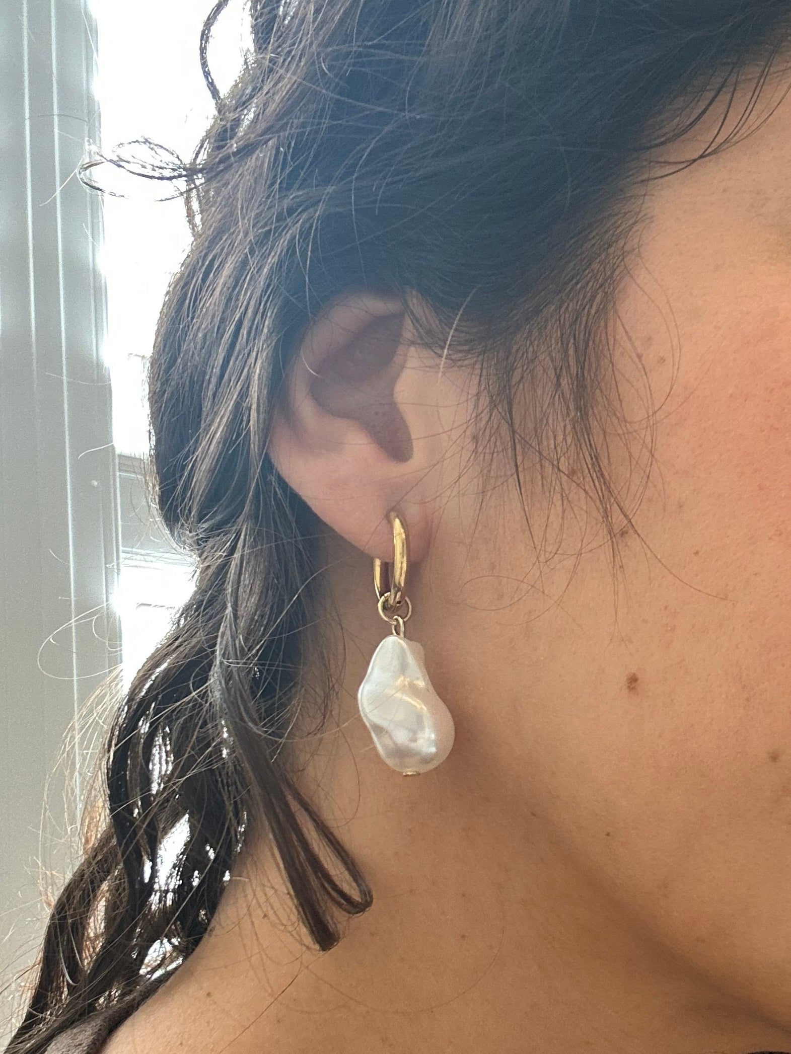 Close-up of a person wearing a gold earring with a clear gemstone.