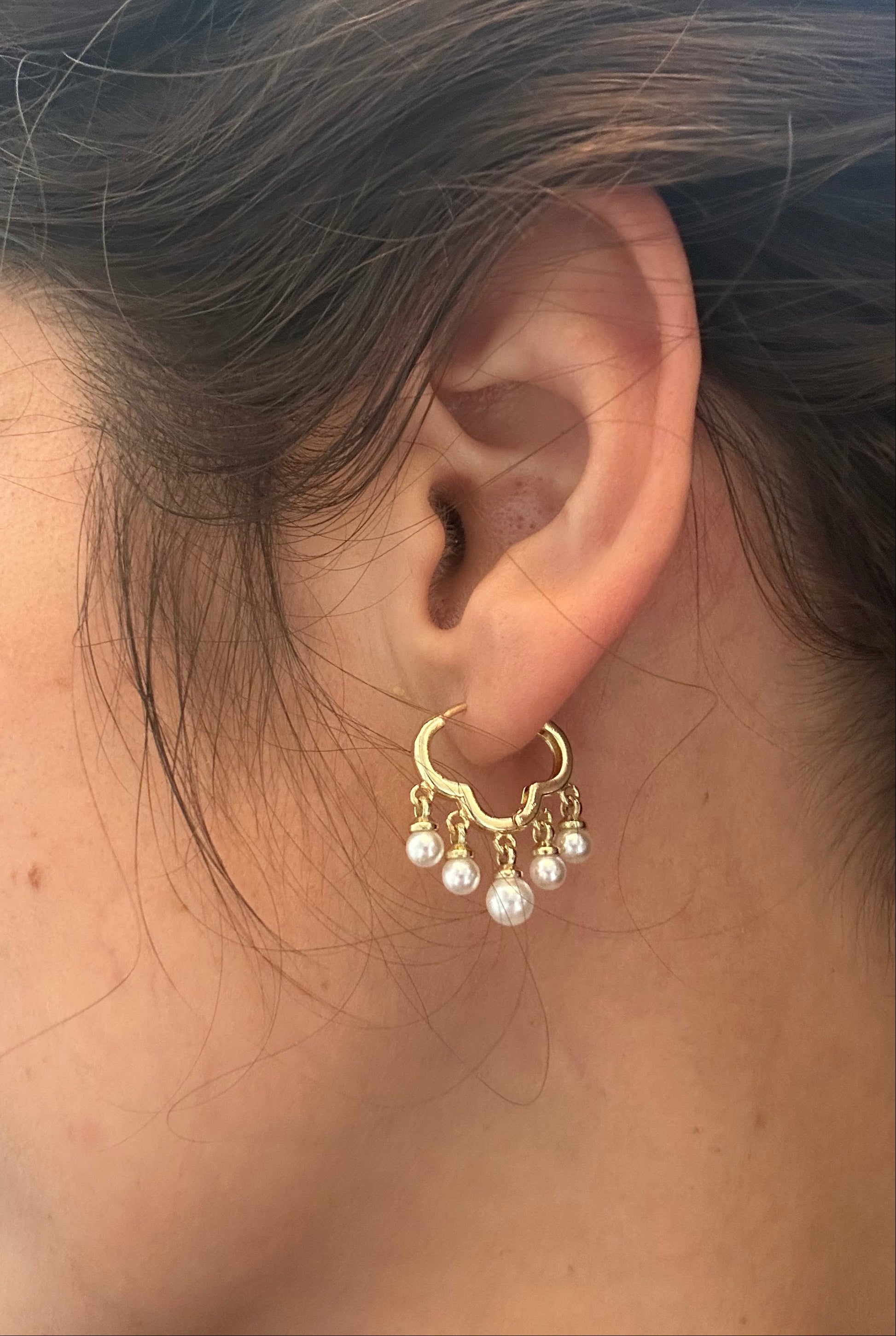Close-up of an ear wearing a gold earring with pearls.