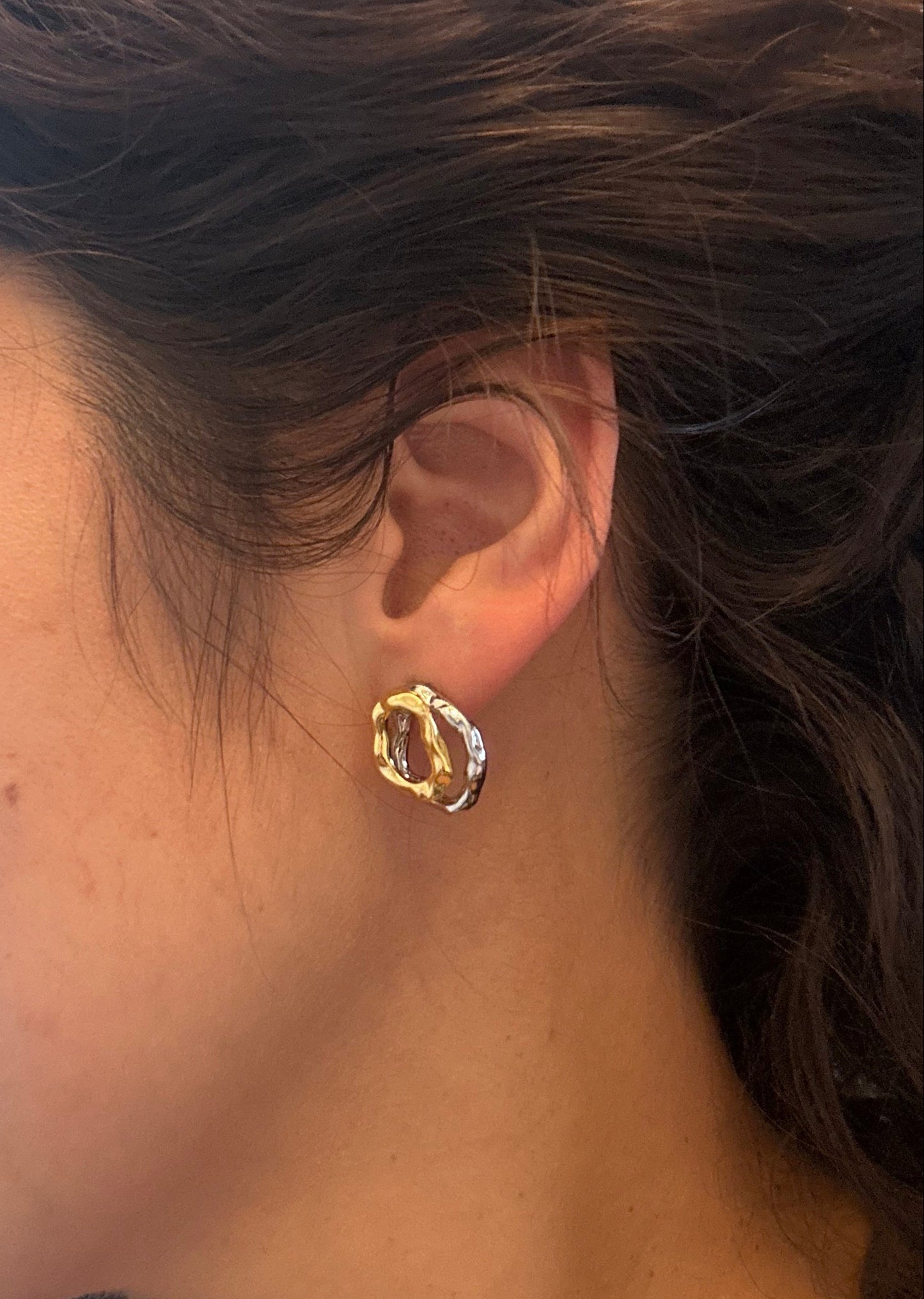 Close-up of an ear wearing a gold earring with a blurred background