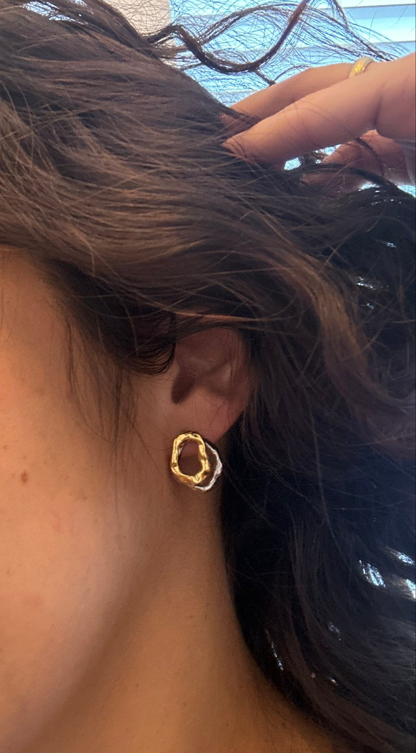 Close-up of a person wearing a gold earring outdoors