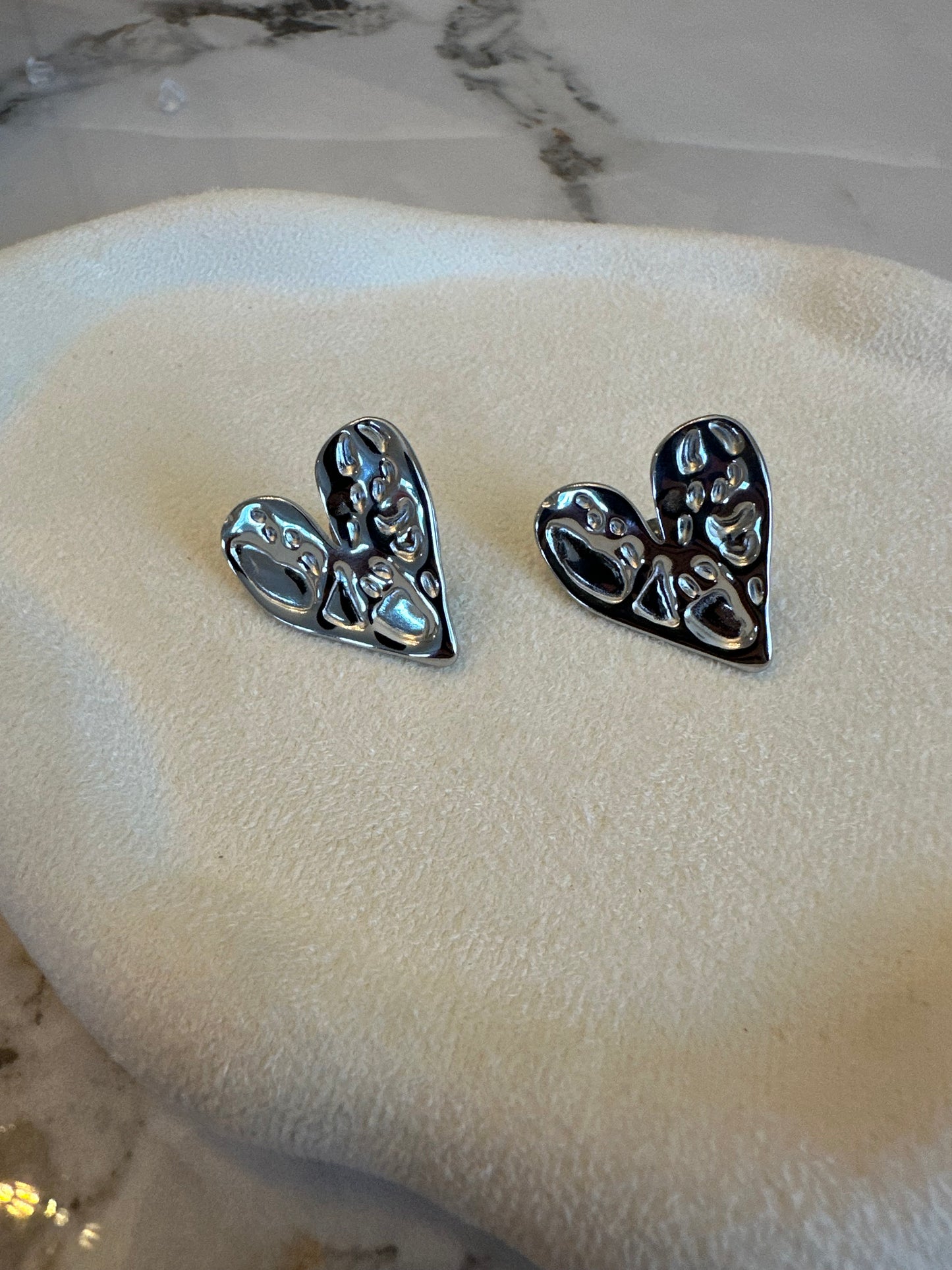 Pair of silver leaf-shaped earrings on a beige cushion with a marble background.