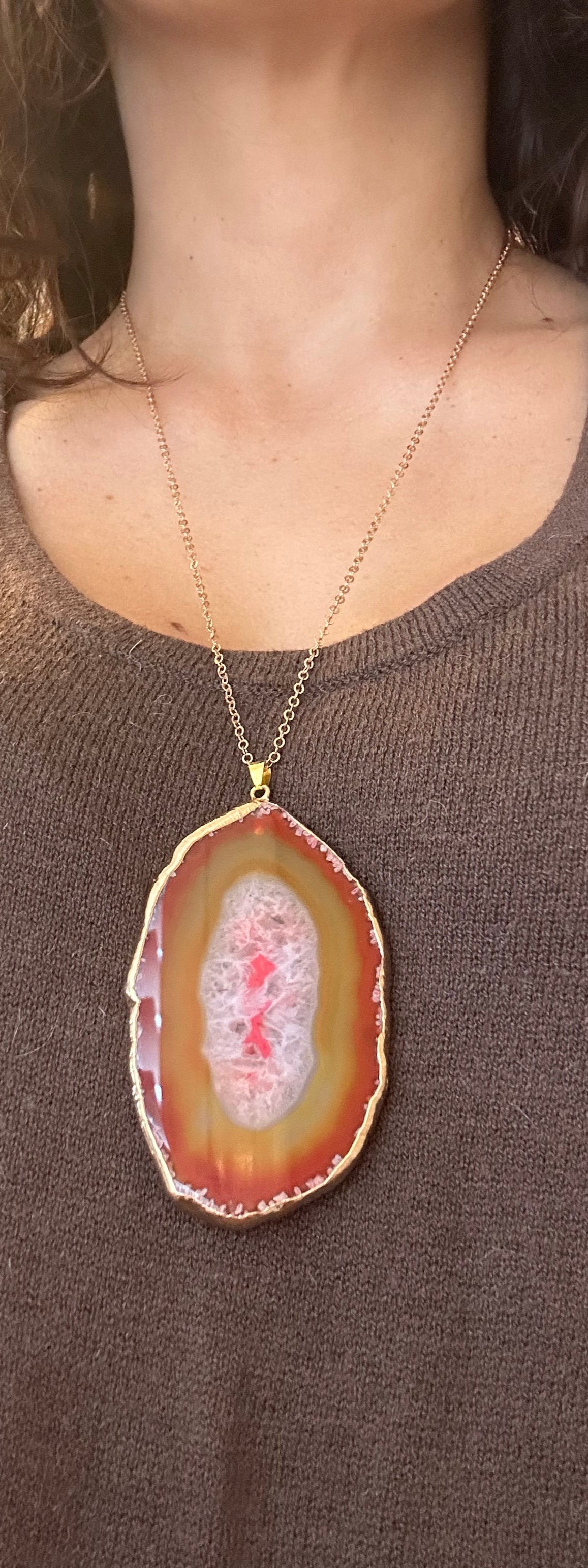 Person wearing a necklace with a large, colorful pendant.