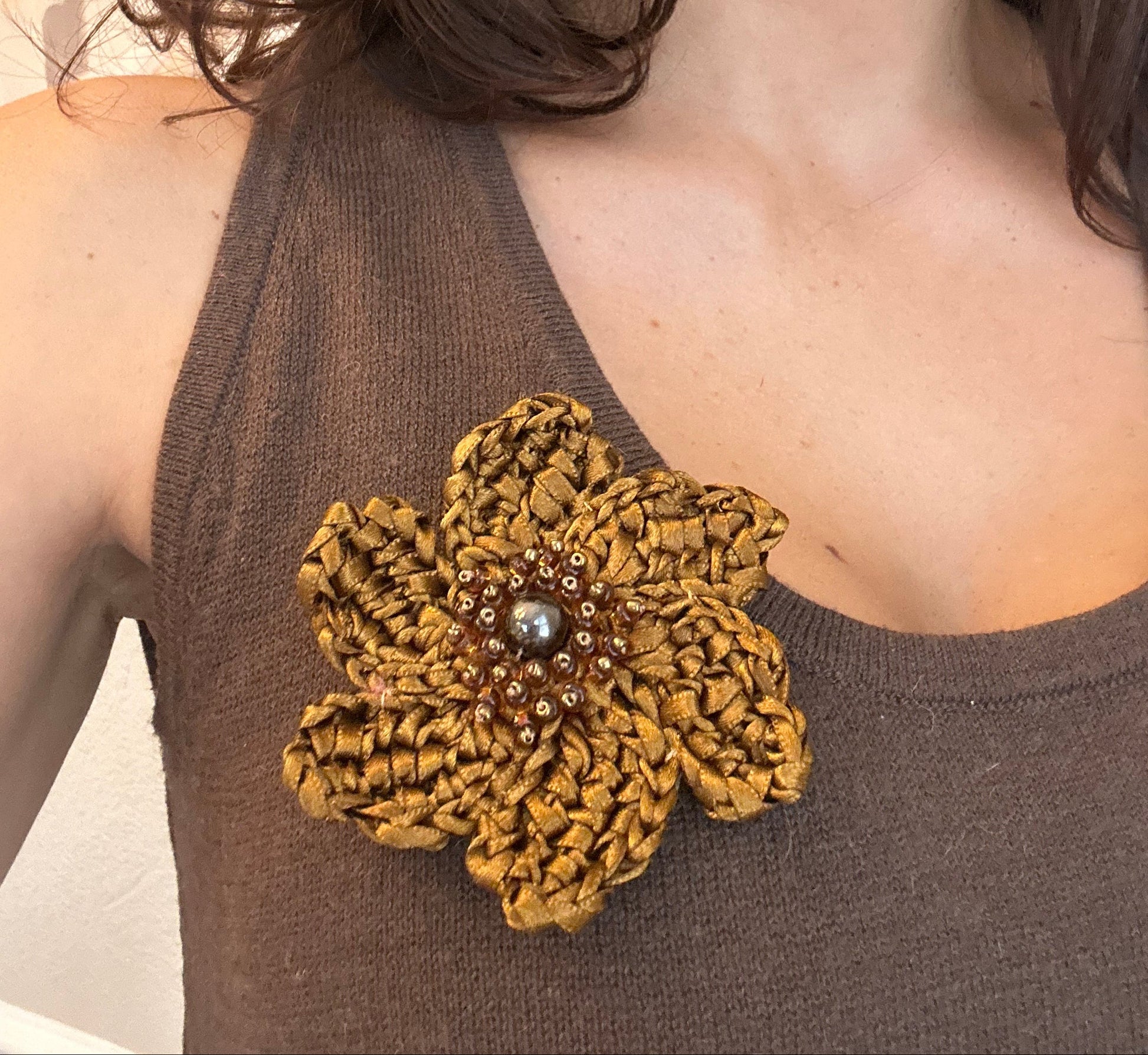 Close-up of a person wearing a brown garment with a decorative flower brooch.