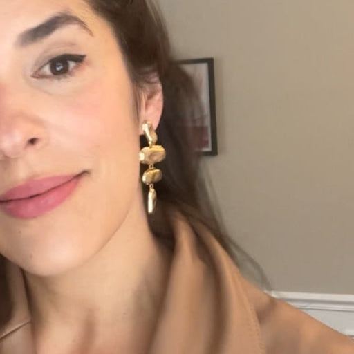 Woman with long dark hair wearing a beige sleeveless top indoors.