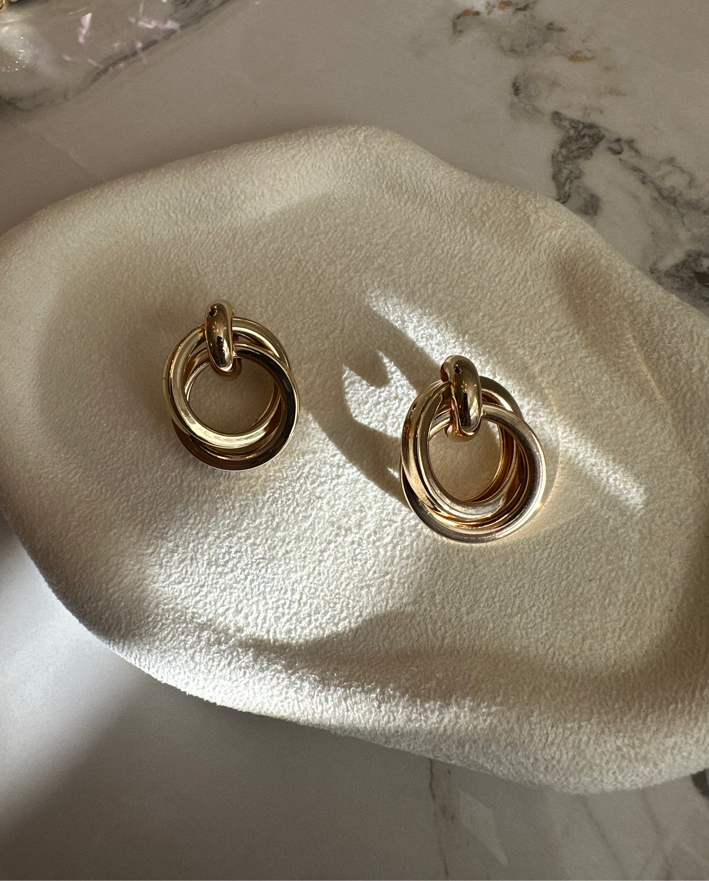 Gold hoop earrings on a white stone surface with marble background