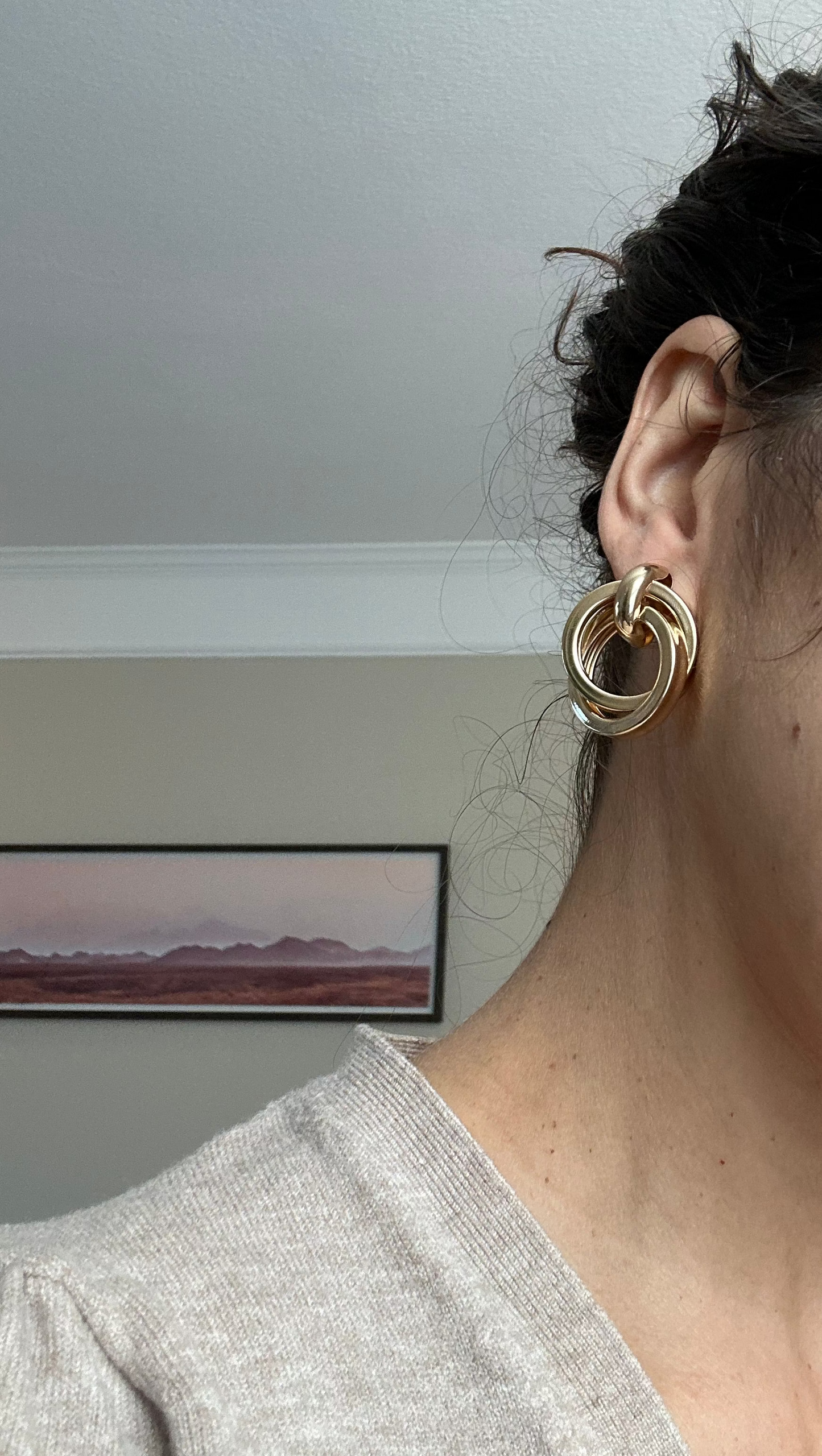 Close-up of a person wearing a gold hoop earring with a neutral background