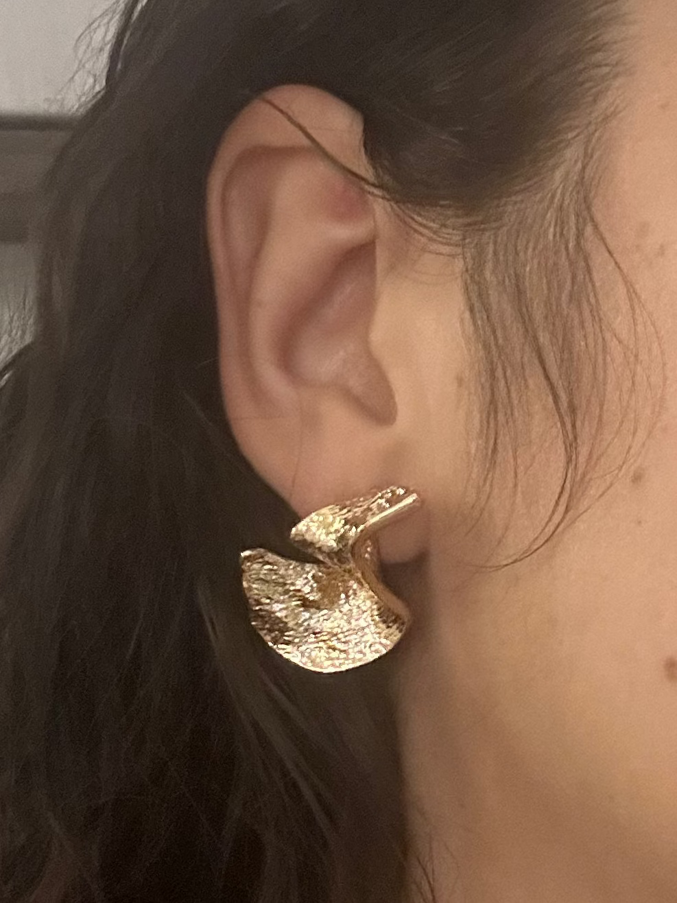 Close-up of a person wearing a gold earring with a neutral background