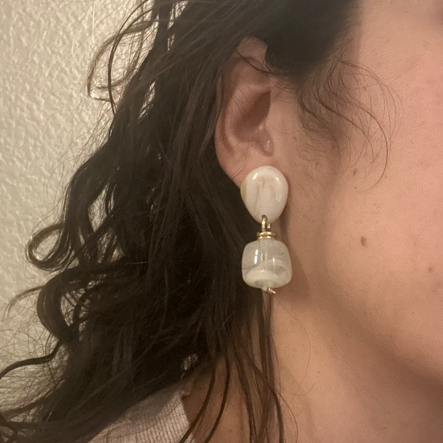 Close-up of a person wearing a pearl earring with a neutral background