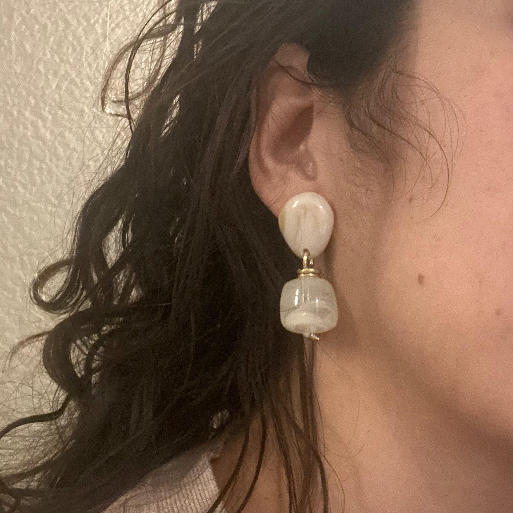 Close-up of a person wearing a pearl earring with a neutral background