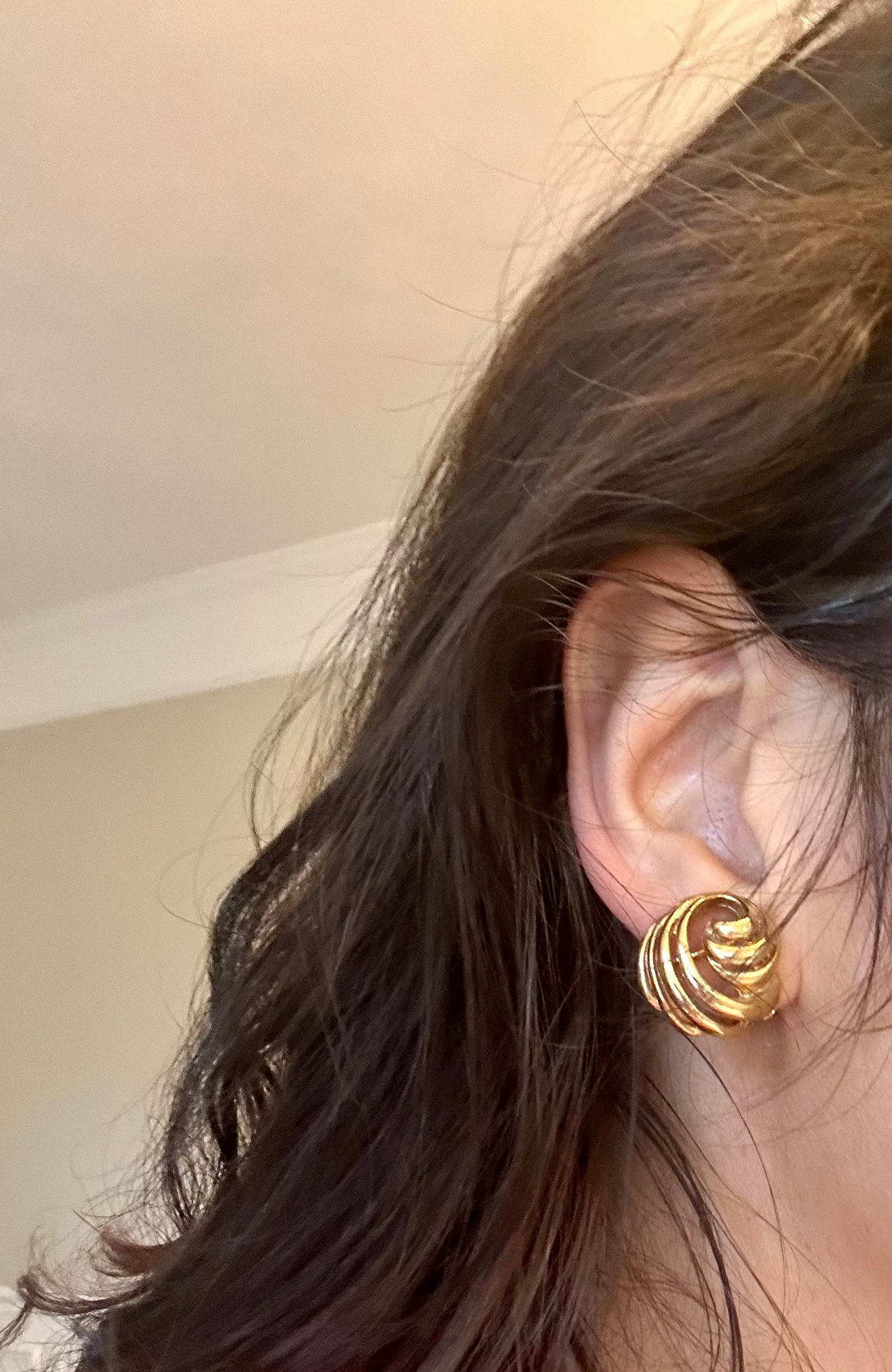 Close-up of a person wearing gold spiral earrings with a neutral background