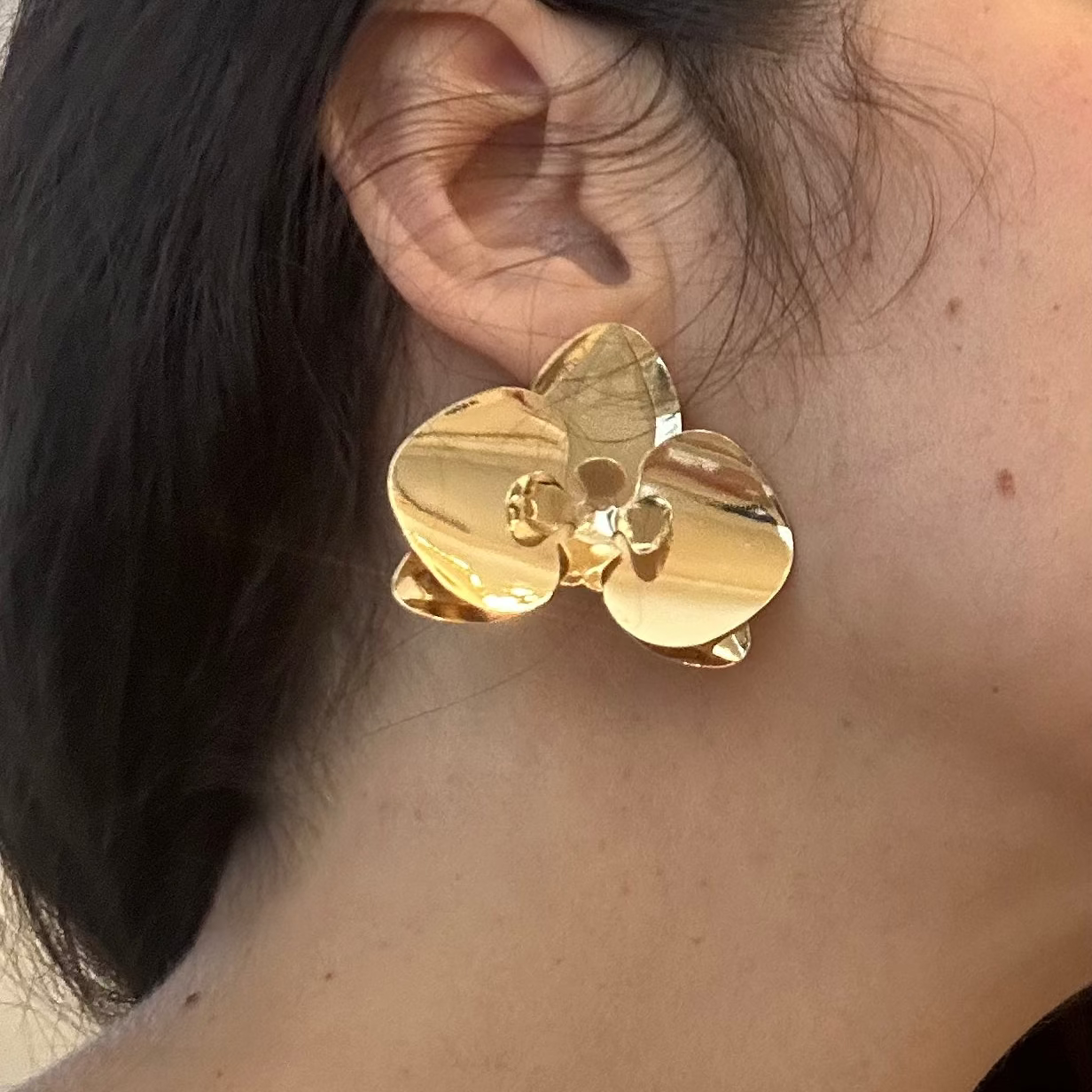 Gold earrings worn by a person with dark hair against a neutral background