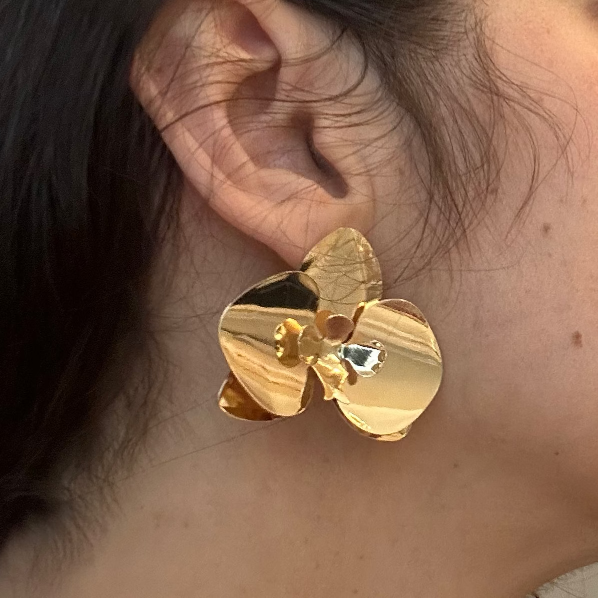 Woman wearing gold earrings in a neutral indoor setting