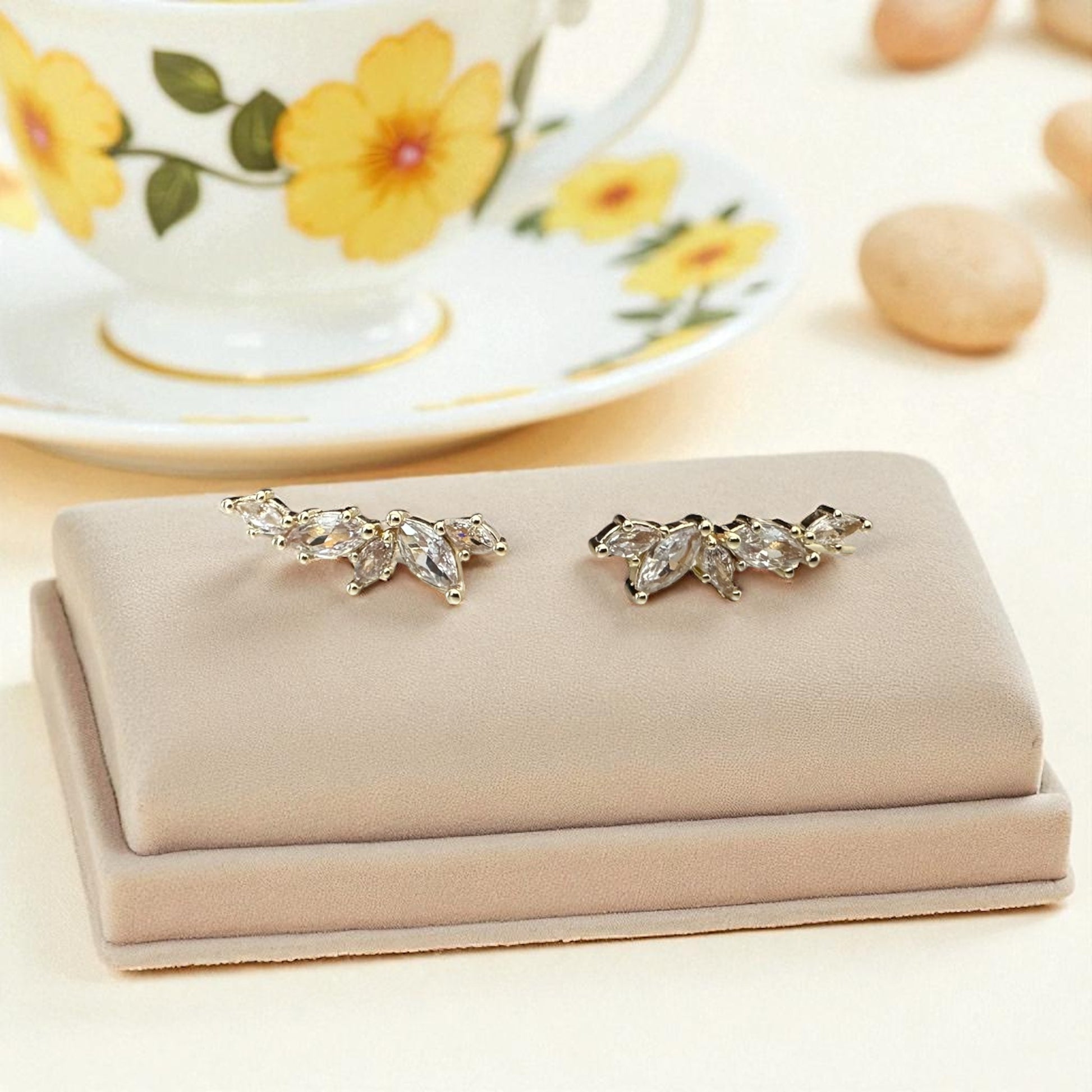 Pair of silver earrings on a beige jewelry display with a floral teacup in the background.